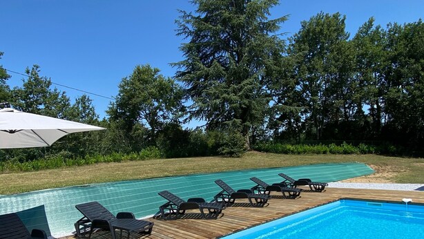 A wooden deck with a swimming pool, surrounded by greenery and trees.