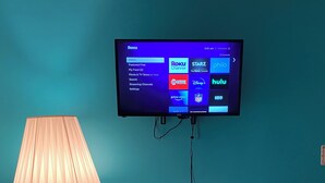 Un téléviseur fixé à un mur de couleur turquoise affiche l’interface Roku et propose différents canaux de diffusion en continu.