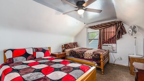 Une chambre avec un lit, un ventilateur de plafond, une fenêtre avec des rideaux et un ventilateur sur pied.