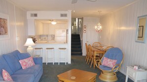 A living room with a blue sofa, a wooden coffee table, and a dining area with wooden chairs and a table. - El Capitan, Ocean City, MD, USA unit 203 located on the boardwalk and ocean at 4th street (Ocean City)