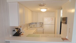 A compact kitchen with white cabinets, a microwave, a refrigerator, and a coffee maker. There are three stools with woven seats. - El Capitan, Ocean City, MD, USA unit 203 located on the boardwalk and ocean at 4th street (Ocean City)