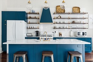 Eine moderne Küche mit blauen Schränken, einer weißen Kochinsel, Edelstahl-Barhocker und verschiedenen Küchengeräten.