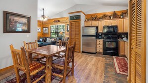 A kitchen with wooden cabinets, a refrigerator, stove, and microwave. There is a dining table with chairs. - 2 Queen BR Cozy Walk-in Log Cabin close to Branson Entertainment (Branson)