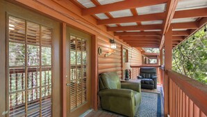 A wooden porch with a covered area, a green leather chair, a small table with a lamp, and a view of trees. - 2 Queen BR Cozy Walk-in Log Cabin close to Branson Entertainment (Branson)