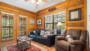 A log cabin interior with a leather sofa, a brown armchair, a wooden coffee table, and framed pictures on the walls. - 2 Queen BR Cozy Walk-in Log Cabin close to Branson Entertainment (Branson)