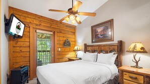 A bedroom with a wooden ceiling fan, a bed with white bedding, a nightstand with a lamp, and a small wooden dresser. - 2 Queen BR Cozy Walk-in Log Cabin close to Branson Entertainment (Branson)
