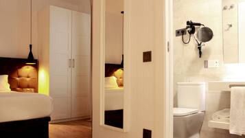 Quarto de hotel com cama, guarda-roupa e banheiro com vaso sanitário e suporte para toalhas.