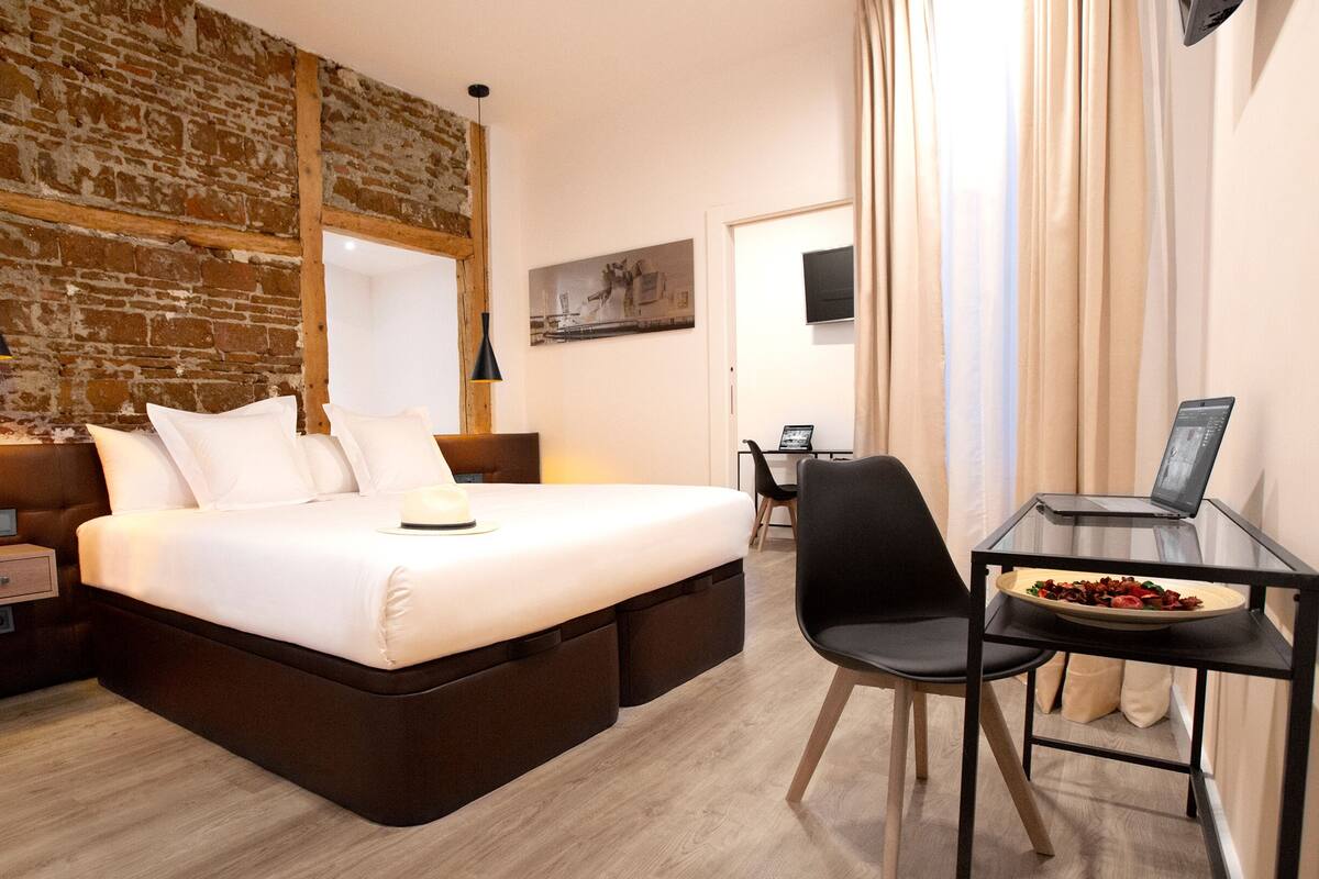 Une chambre d’hôtel moderne avec un grand lit, un bureau avec un ordinateur portable et un coin repas avec une assiette de nourriture.