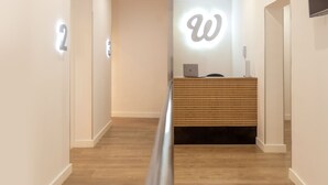 A reception desk with a wooden panel design, a large illuminated 'W' sign, and a laptop on the desk. - Woohoo Rooms Fuencarral (Madrid)