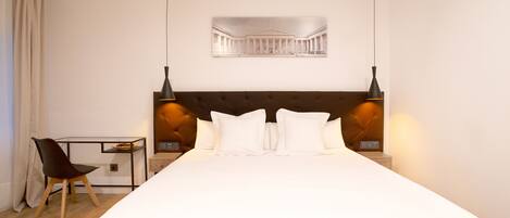 Habitación de hotel con una cama grande, un escritorio, una silla y dos lámparas fijadas a la pared.