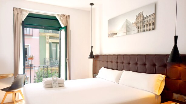 A hotel room with a large bed, a balcony with a view of a building, and a painting on the wall. - Woohoo Rooms Fuencarral (Madrid)