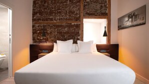A hotel room with a large bed, a brick wall, and a painting on the wall. - Woohoo Rooms Fuencarral (Madrid)