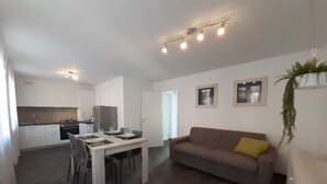 Una cocina moderna con armarios blancos, una mesa de comedor preparada para cuatro personas y un sofá con un cojín amarillo.