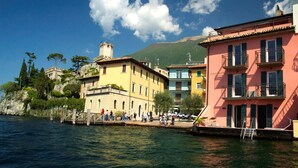 Una propiedad frente al agua con muelle, edificios con balcones y una montaña al fondo.