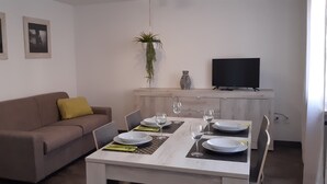 Una sala de estar con un sofá, una mesa de comedor para dos personas, un televisor y cuadros en la pared.