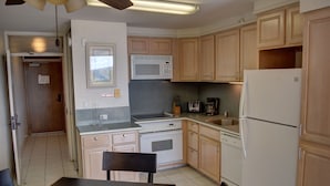A compact kitchen with wooden cabinets, a microwave, a stove, a sink, and a refrigerator. - 7th Floor Oceanfront Condo at Mana Kai Resort (Kihei)