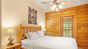 Un dormitorio con paneles de madera, una cama, mesitas de noche, un ventilador de techo y una ventana con persianas.
