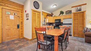 Un comedor con mesa y sillas de madera, una cocina con armarios de madera, un reloj en la pared y una puerta con cerradura.