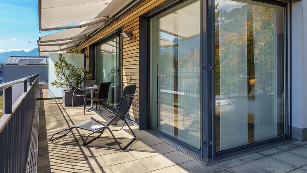 Un balcón moderno con puerta de cristal, una mesa, sillas y una planta en maceta.
