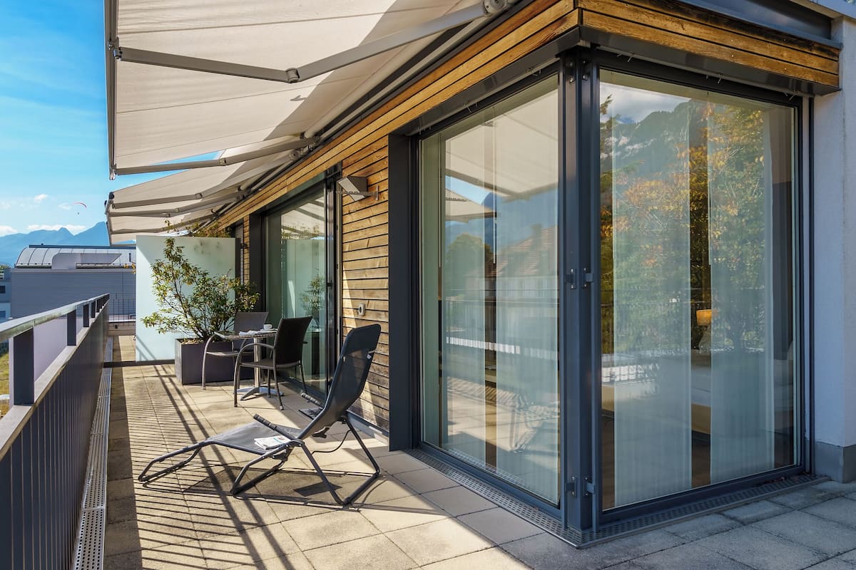 A modern balcony with a glass door, a table, chairs, and a potted plant.
