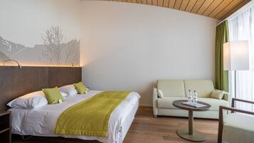 Habitación de hotel con cama, sofá, una mesa redonda con dos botellas y una lámpara.