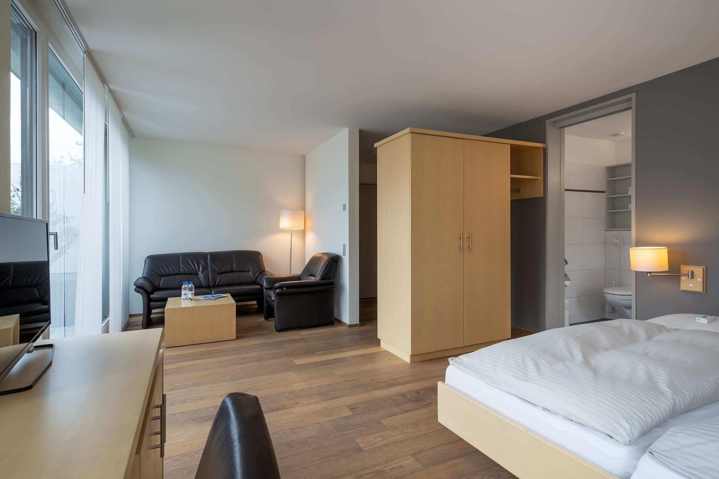 A modern hotel room with a bed, a sofa, a desk, and a wardrobe.