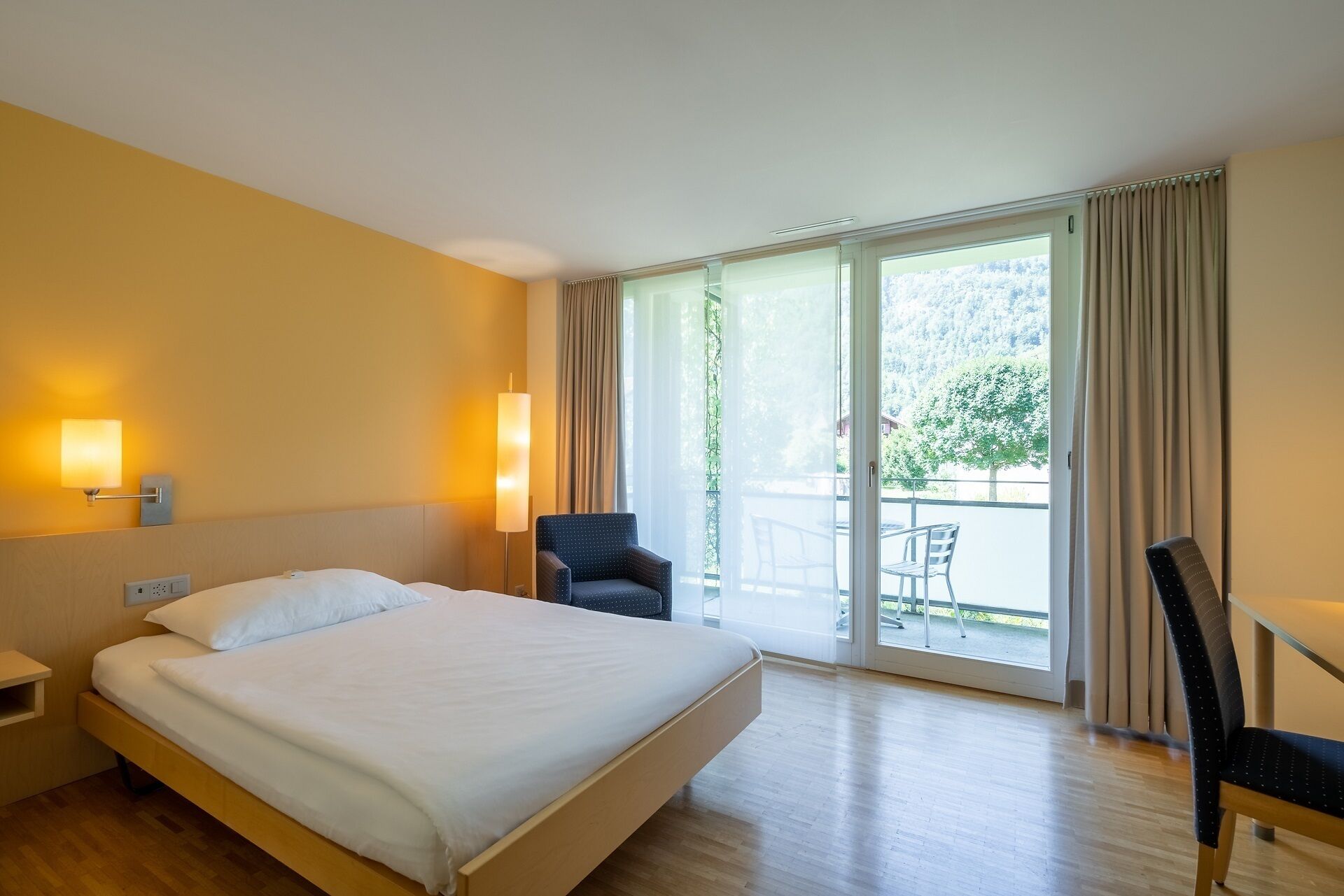 Una habitación de hotel con una cama, una silla, un escritorio y vistas al exterior.