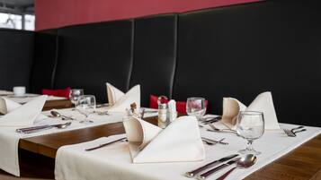 A restaurant table set with white tablecloth, silverware, and wine glasses, with a black cushioned booth in the background.