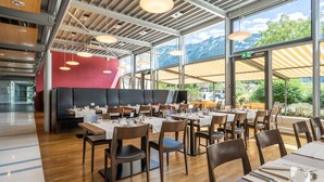 Un restaurante moderno con suelo de madera, asientos acolchados negros y amplias ventanas con vistas a la montaña.