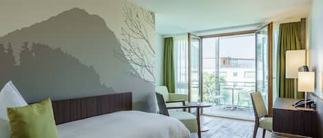 Habitación de hotel con cama, escritorio, silla, una mesita y vista al exterior.