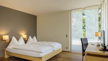 Habitación de hotel moderna con cama, lámparas de noche, escritorio y vistas a zonas verdes a través de amplios ventanales.