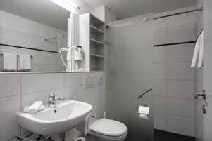 Un baño moderno con lavamanos, inodoro y ducha blancos.