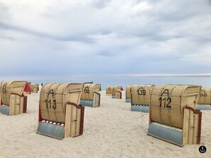 Beach huts numbered 131, 139, 150, and 112 on a sandy beach with the sea in the background.