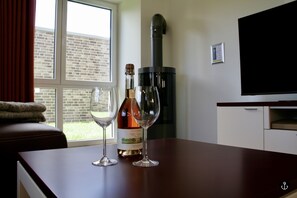 A room with a wooden table, two wine glasses, a wine bottle, a fireplace, a TV, and a window with curtains.