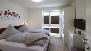 Ein Schlafzimmer mit einem Bett, einem Fernseher, einem Fenster und einem Bild an der Wand.