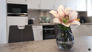 Eine Küche mit weißen Schränken, einer schwarzen Mikrowelle, einem Backofen und einer Vase mit einer Blume auf der Arbeitsfläche.