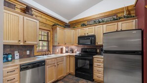 Una cocina con armarios de madera, un lavavajillas de acero inoxidable, una estufa negra, un microondas y un refrigerador.