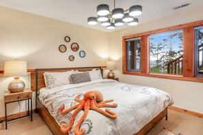 A bedroom with a large bed, a wooden headboard, a window with a view of trees, and a ceiling light fixture.