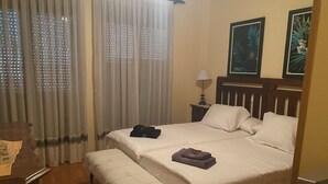 Habitación de hotel con cama, mesita de noche con lámpara, banco y cortinas con estampado.