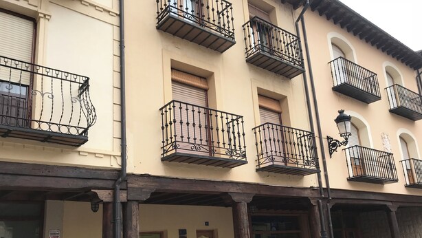 Un edificio con varios balcones, vigas de madera y un banco a la calle.