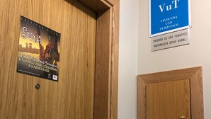 Una puerta de madera con un cartel publicitando un tour en Soria, un letrero azul que indica una zona de uso turístico, y un pequeño panel de madera en la pared.