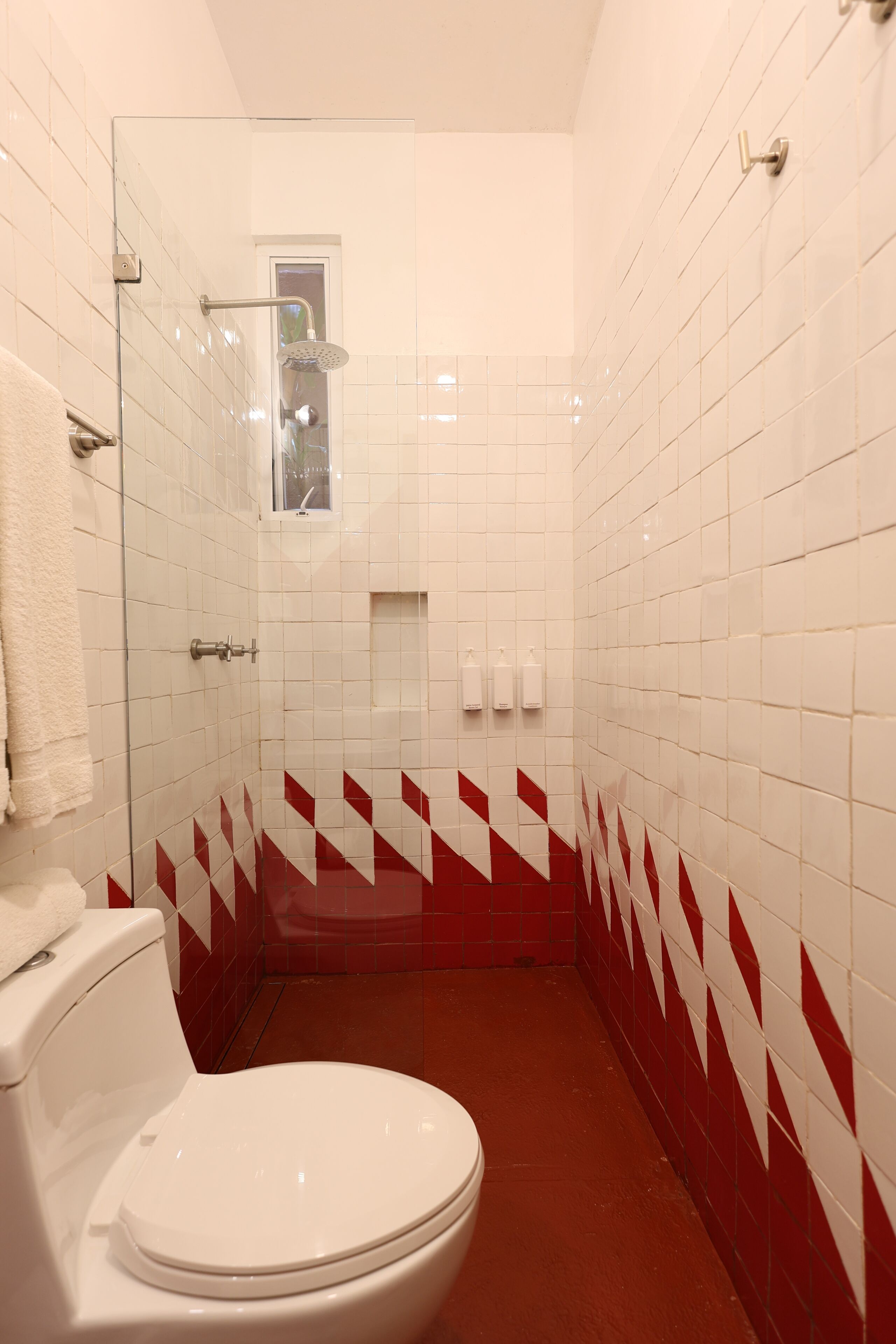 Uma casa de banho com sanita branca, cabine de duche em vidro e azulejos xadrez vermelhos e brancos.