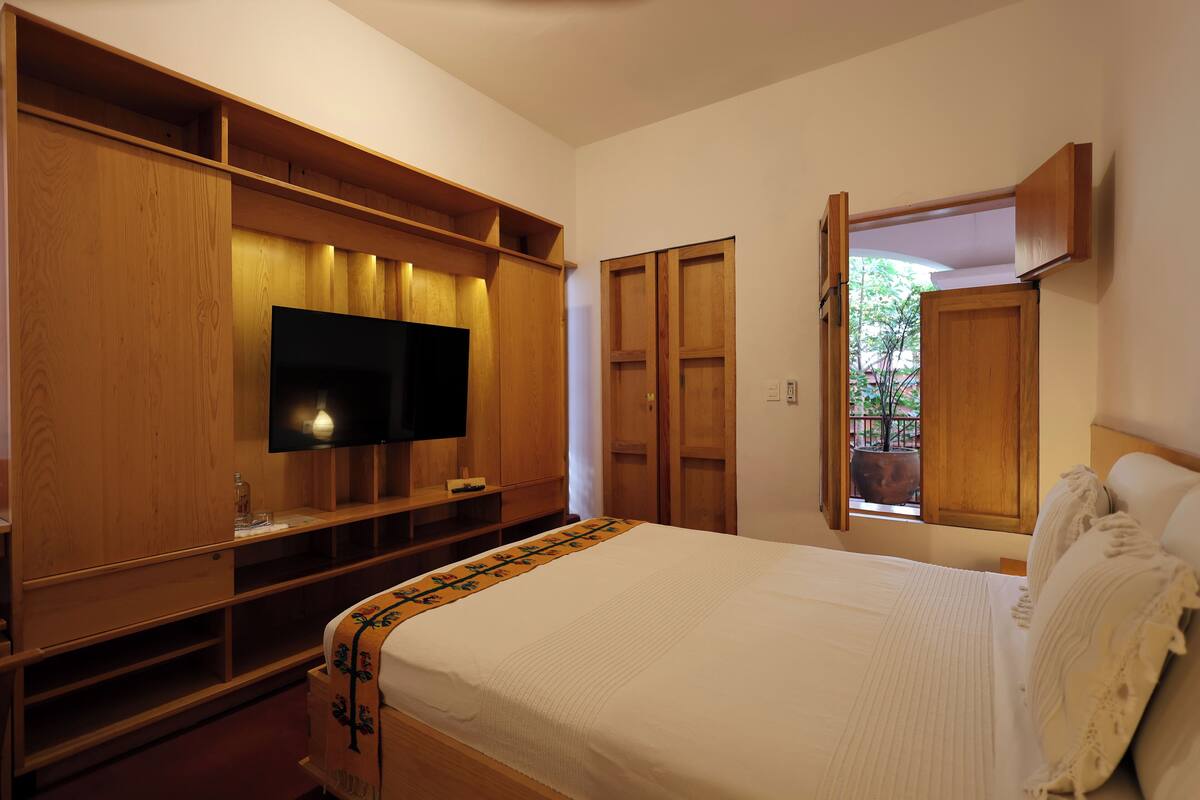 A bedroom with a bed, wooden wardrobe, TV, and a window with a view.