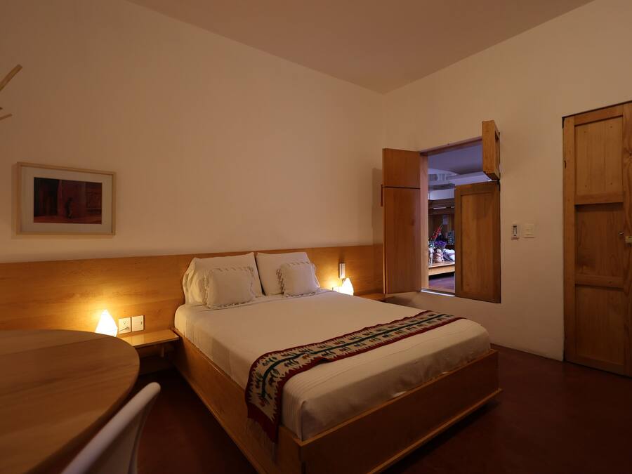 A bedroom with a bed, bedside lamps, a wooden headboard, a wooden wardrobe, and a framed picture on the wall.