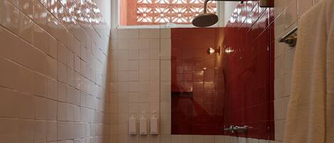 Casa de banho pequena com azulejos brancos e vermelhos, sanita, chuveiro e janela com um painel decorativo.
