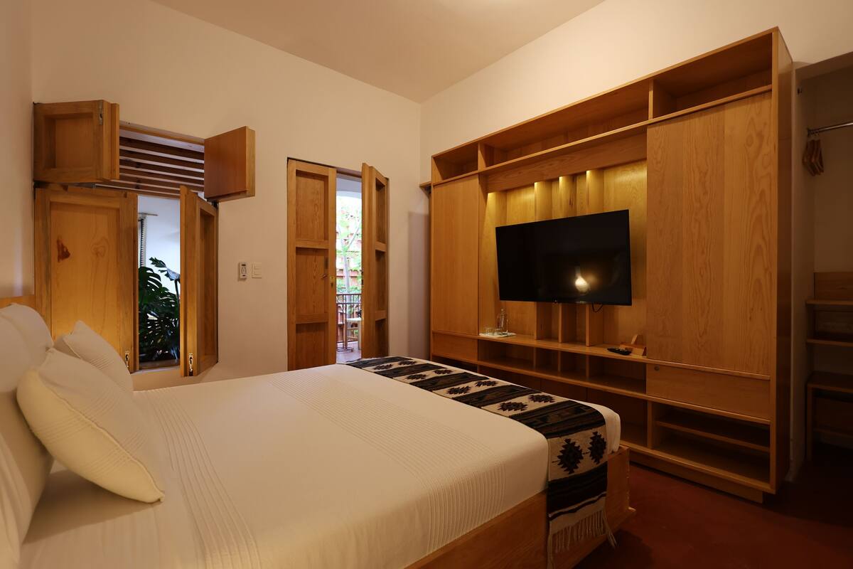 A bedroom with a large bed, wooden wardrobe, and a TV.