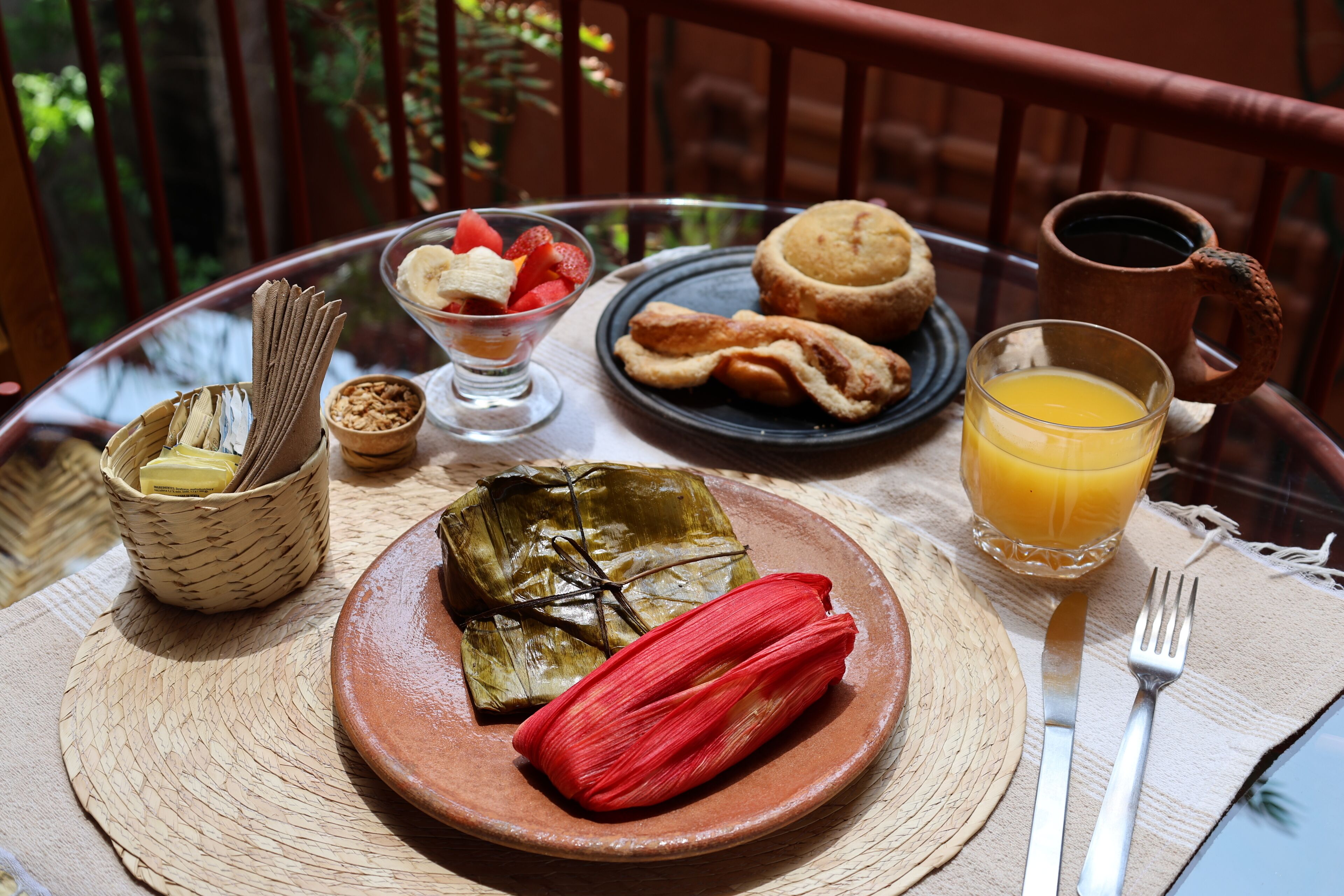 A table with a plate of tamales, a glass of orange juice, a cup of coffee, and a basket of bread.