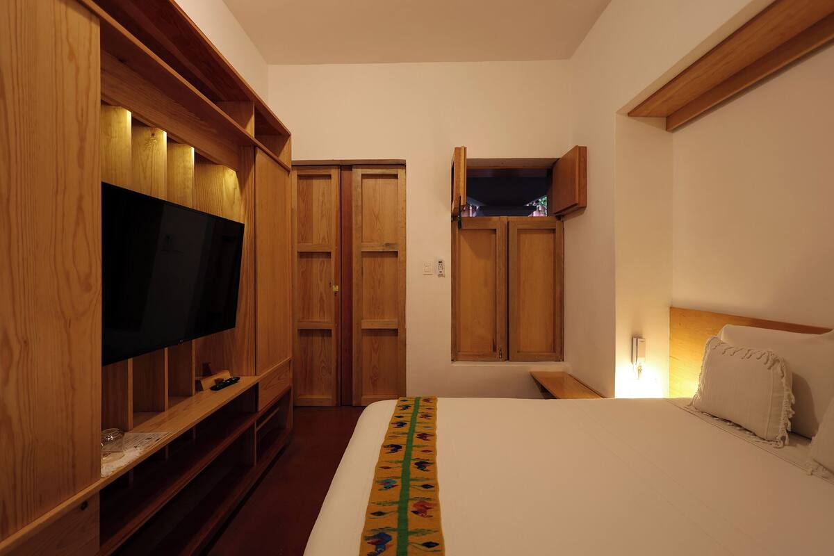 A bedroom with a bed, a TV, wooden wardrobe, and a nightstand.