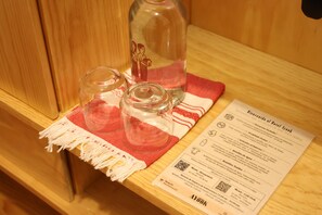 A wooden table with a glass bottle, two glasses, and a red and white cloth. A printed paper with text and QR codes is also visible.