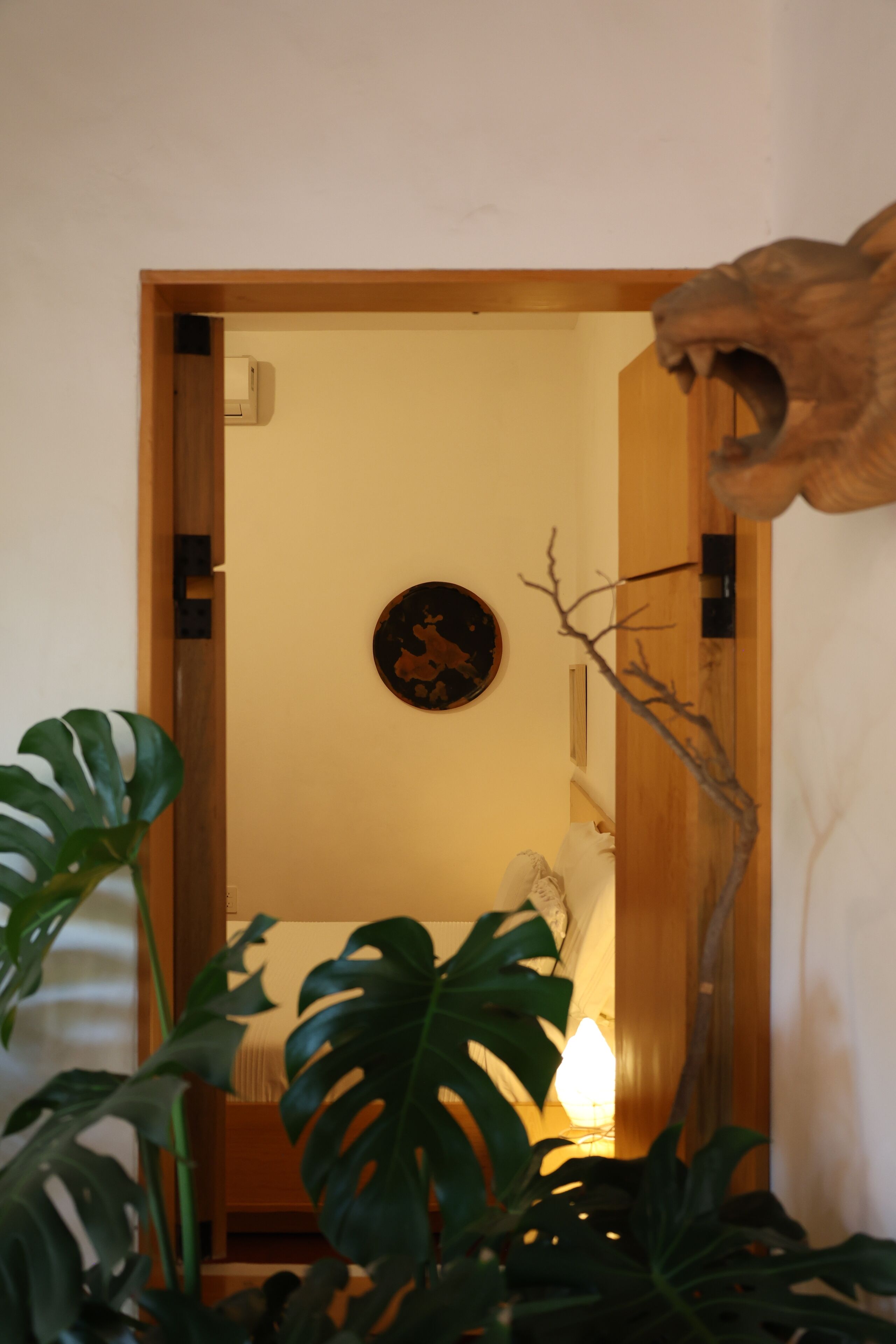 Una habitación con una puerta de madera, un adorno en la pared y una planta en primer plano.